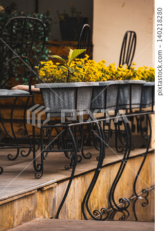 Charming Outdoor Cafe Terrace with Wrought Iron Furniture and Yellow Flower Planters Charming Outdoor Cafe Terrace with Wrought Iron Furniture and Yellow Flower Planters 140218280