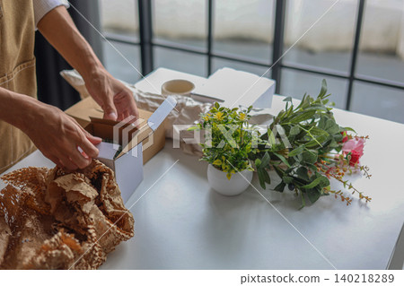 A small business, a florist or a gift shop worker preparing, wrapping, packing a customer's order. A small business, a florist or a gift shop worker preparing, wrapping, packing a customer's order. 140218289