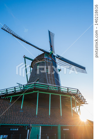 Traditional dutch windmill undeTraditional dutch windmill under clear br clear blue sky with bright sunburst, historic wooden mill structure with lens flare and copy space in zaanse schans netherlands Traditional dutch windmill undeTraditional dutch windmill under clear br clear blue sky with bright sunburst, historic wooden mill structure with lens flare and copy space in zaanse schans netherlands 140218616