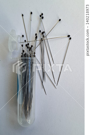 A clear plastic container is filled with metal sewing insect pins with black heads. Some pins are scattered outside the container on a flat surface. This setup is typical for entomology collections. A clear plastic container is filled with metal sewing insect pins with black heads. Some pins are scattered outside the container on a flat surface. This setup is typical for entomology collections. 140218973