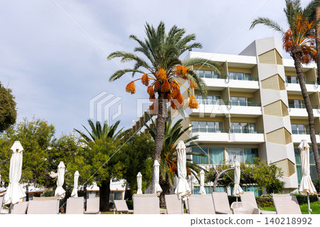 Fruiting date palm and oleander in front of a modern Mediterranean resort hotel facade with balconies in Paphos, Cyprus. Fruiting date palm and oleander in front of a modern Mediterranean resort hotel facade with balconies in Paphos, Cyprus. 140218992