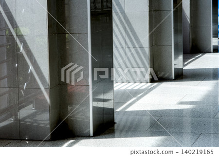 Modern architectural design featuring polished grey stone pillars and geometric shadows cast on a tiled floor in a minimalist building corridor Modern architectural design featuring polished grey stone pillars and geometric shadows cast on a tiled floor in a minimalist building corridor 140219165