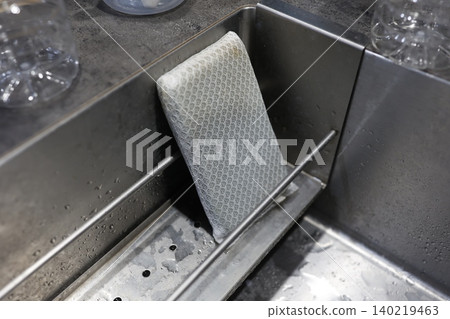 廚房水槽。網狀洗碗海綿。一塊略微髒污的海綿放在不鏽鋼水槽上。 140219463