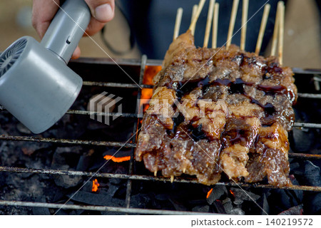 Closeup of raw meat skewers being grilled over charcoal with a culinary torch for extra char and flavor Closeup of raw meat skewers being grilled over charcoal with a culinary torch for extra char and flavor 140219572