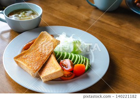 A breakfast plate of toast, avocado, and tomato, along with a warm soup. 140221182