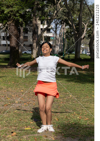 A teenager in a white shirt and orange skirt is smiling and jumping in the grass A teenager in a white shirt and orange skirt is smiling and jumping in the grass 140221228