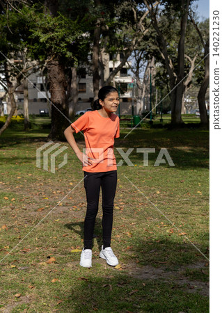A young girl in an orange shirt stands in a park 140221230