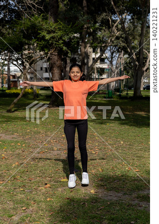 A girl in an orange shirt is standing in a park A girl in an orange shirt is standing in a park 140221231