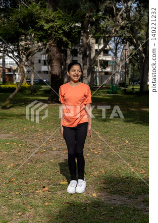 A young girl in an orange shirt is standing in a park A young girl in an orange shirt is standing in a park 140221232