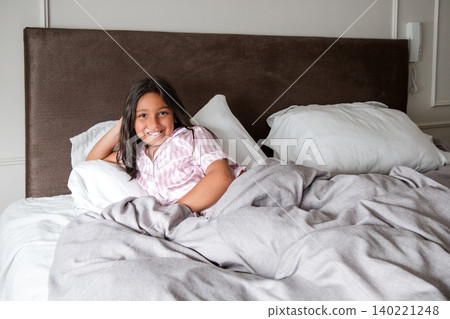 A young girl is laying on a bed with a blanket and a pillow A young girl is laying on a bed with a blanket and a pillow 140221248