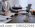 professional lawyer writing legal document notes at office desk with justice scales gavel and laptop computer working on case research consultation in modern 140222544