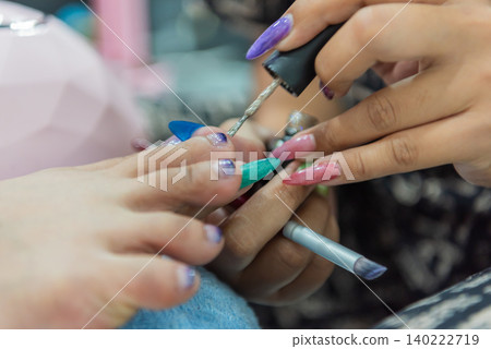 Professional nail technician applying polish during colorful manicure session featuring long acrylic nails beauty care fashion style salon services 140222719
