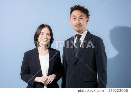 A light blue background features a smiling businessman and businessman in suits, looking directly at the camera, conveying a B2B image of success and challenge. A light blue background features a smiling businessman and businessman in suits, looking directly at the camera, conveying a B2B image of success and challenge. 140223096