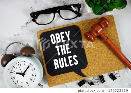 Obey The Rules text on speech bubble with alarm clock and wooden gavel on marble background Obey The Rules text on speech bubble with alarm clock and wooden gavel on marble background 140223319