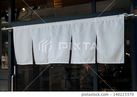 A plain white noren (curtain) hanging at the entrance of a restaurant. 140223370