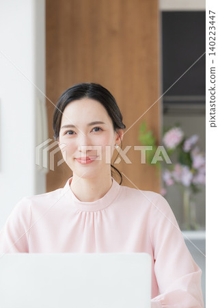 一位身穿粉紅色洋裝的美麗女子坐在辦公桌前,正在使用電腦工作,並直視鏡頭。 一位身穿粉紅色洋裝的美麗女子坐在辦公桌前,正在使用電腦工作,並直視鏡頭。 140223447