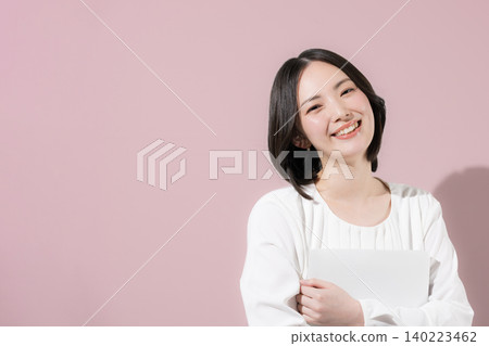 A cute, smiling female employee with a laptop against a pink background, looking directly at the camera in a business image; suitable for job changes and career development. A cute, smiling female employee with a laptop against a pink background, looking directly at the camera in a business image; suitable for job changes and career development. 140223462