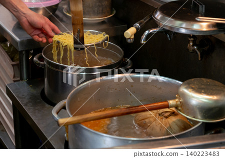 拉麵店廚房裡的烹飪場景,麵條用扁平的濾網從大鍋子裡撈出來。 拉麵店廚房裡的烹飪場景,麵條用扁平的濾網從大鍋子裡撈出來。 140223483