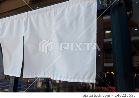 A plain white noren (curtain) hanging in front of a restaurant. 140223553