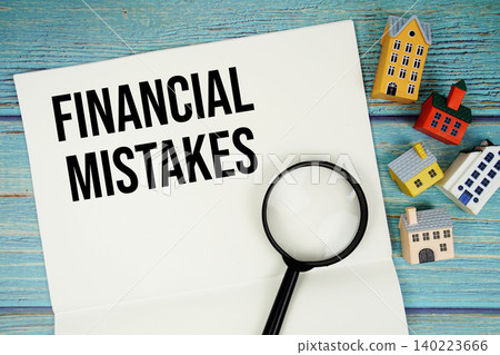 Notepad with "Financial Mistakes" with magnifying glass and house model on wooden background 140223666