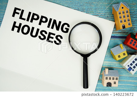 Notepad with "Flipping Houses" with magnifying glass and house model on wooden background 140223672