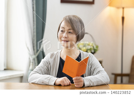 A senior woman looking at her pension book in the living room A senior woman looking at her pension book in the living room 140223852