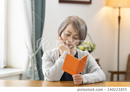 A senior woman looking at her pension book in the living room A senior woman looking at her pension book in the living room 140223855