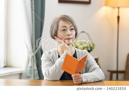 A senior woman looking at her pension book in the living room A senior woman looking at her pension book in the living room 140223858