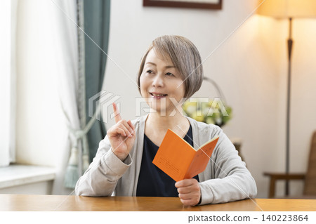 A senior woman looking at her pension book in the living room A senior woman looking at her pension book in the living room 140223864