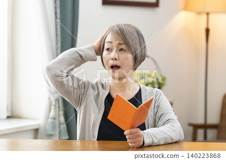 A senior woman looking at her pension book in the living room A senior woman looking at her pension book in the living room 140223868