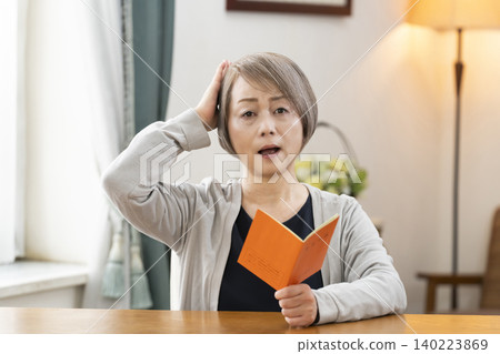 一位老婦人在客廳看著她的退休金手冊。 140223869