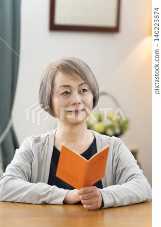 A senior woman looking at her pension book in the living room A senior woman looking at her pension book in the living room 140223874