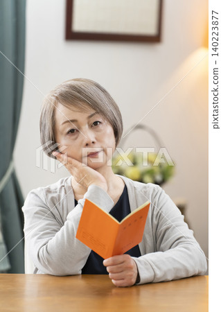 一位老婦人在客廳看著她的退休金手冊。 一位老婦人在客廳看著她的退休金手冊。 140223877