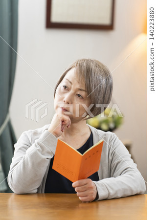 A senior woman looking at her pension book in the living room A senior woman looking at her pension book in the living room 140223880