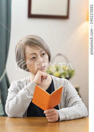 A senior woman looking at her pension book in the living room A senior woman looking at her pension book in the living room 140223882