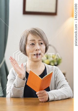 A senior woman looking at her pension book in the living room A senior woman looking at her pension book in the living room 140223890