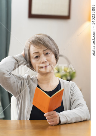 A senior woman looking at her pension book in the living room A senior woman looking at her pension book in the living room 140223893