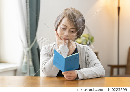 A senior woman looking at her pension book in the living room A senior woman looking at her pension book in the living room 140223899