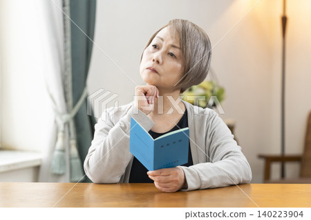 A senior woman looking at her pension book in the living room A senior woman looking at her pension book in the living room 140223904