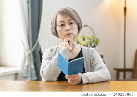 A senior woman looking at her pension book in the living room A senior woman looking at her pension book in the living room 140223905