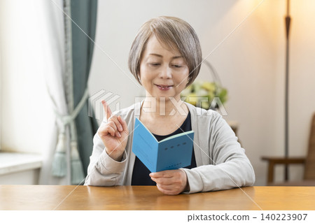 A senior woman looking at her pension book in the living room A senior woman looking at her pension book in the living room 140223907