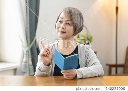 A senior woman looking at her pension book in the living room A senior woman looking at her pension book in the living room 140223908