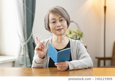 一位老婦人在客廳看著她的退休金手冊。 140223909