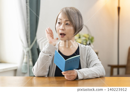 一位老婦人在客廳看著她的退休金手冊。 一位老婦人在客廳看著她的退休金手冊。 140223912