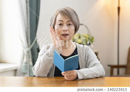 A senior woman looking at her pension book in the living room A senior woman looking at her pension book in the living room 140223913