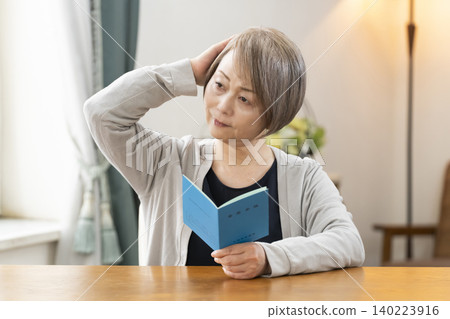 一位老婦人在客廳看著她的退休金手冊。 一位老婦人在客廳看著她的退休金手冊。 140223916