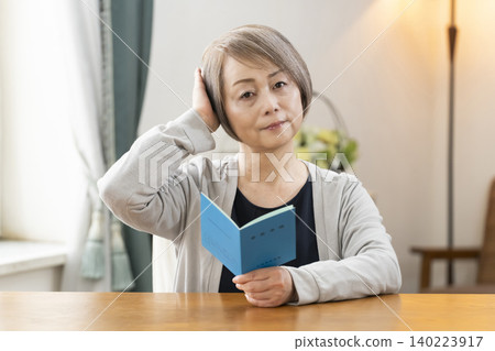 A senior woman looking at her pension book in the living room A senior woman looking at her pension book in the living room 140223917