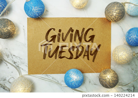 Giving Tuesday text written on paper card with LED cotton balls decorations on marble background Giving Tuesday text written on paper card with LED cotton balls decorations on marble background 140224214