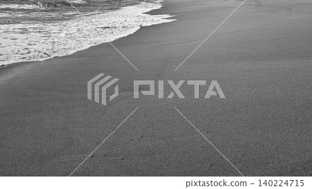 Monochrome high angle view captures glistening ocean water foam washing onto a dark textured sandy beach shore. Beautiful black white minimalist coastal photography highlights a crisp diagonal Monochrome high angle view captures glistening ocean water foam washing onto a dark textured sandy beach shore. Beautiful black white minimalist coastal photography highlights a crisp diagonal 140224715
