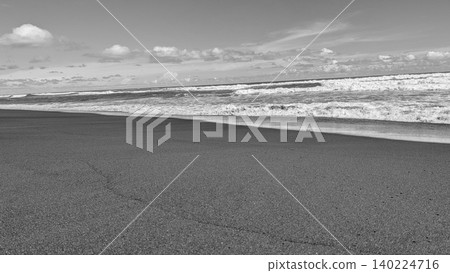 Monochrome wide angle landscape view captures foaming ocean waves breaking on a fine dark sandy beach shore under a bright cloudy sky. Beautiful black white minimalist coastal scenery showcases Monochrome wide angle landscape view captures foaming ocean waves breaking on a fine dark sandy beach shore under a bright cloudy sky. Beautiful black white minimalist coastal scenery showcases 140224716